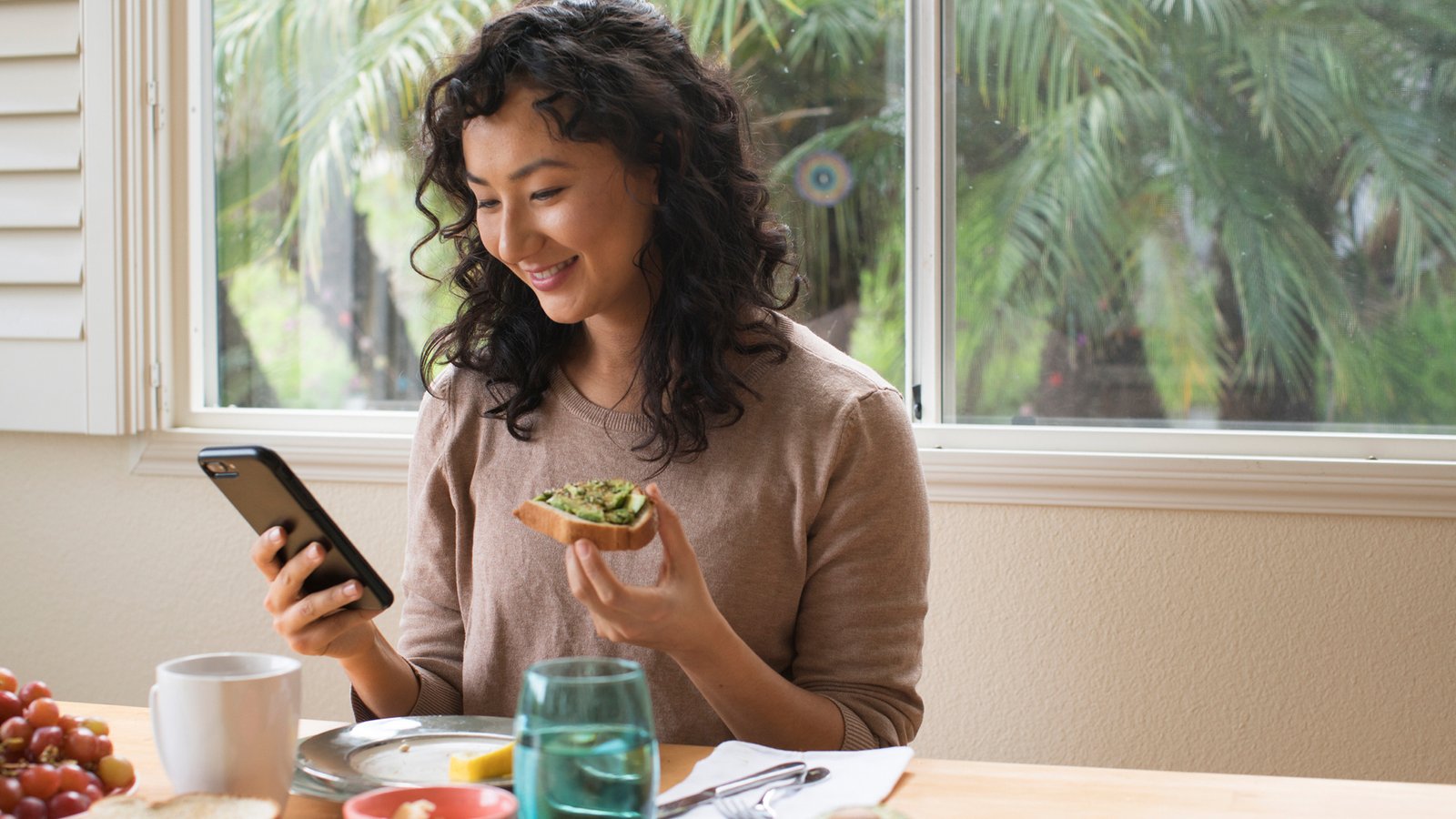 femme mangeant de l’avocat sur du pain grillé tout en regardant son téléphone