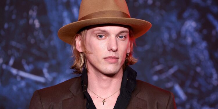 L'image peut contenir des vêtements des vêtements un chapeau Jamie Campbell Bower une personne un chapeau de soleil un costume un pardessus et un manteau