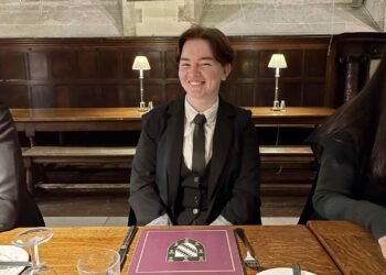 L'image peut contenir une personne humaine, des meubles en bois, des vêtements de table, des vêtements, un manteau, un pardessus et une table.