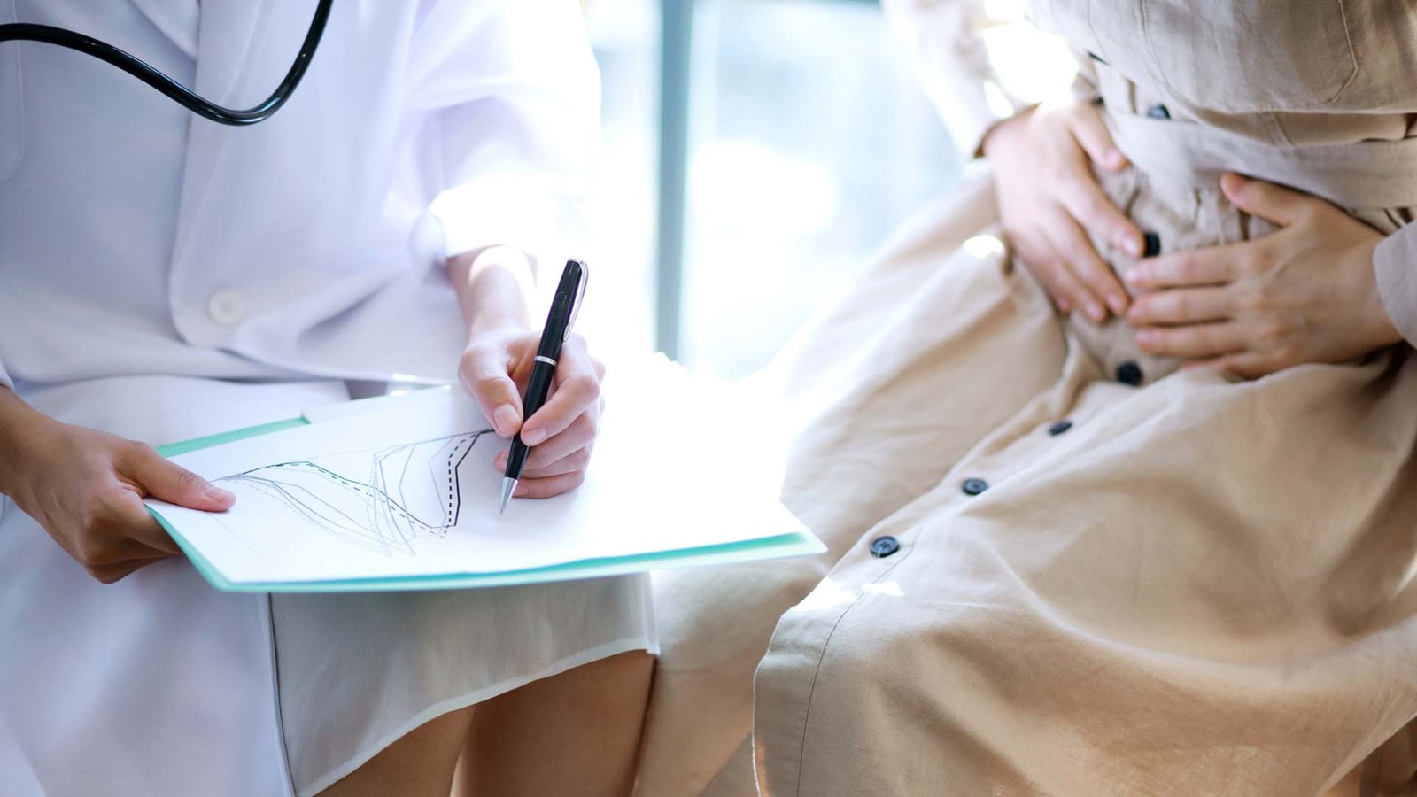 femme tenant son estomac alors qu'un médecin diagnostique sa douleur à l'estomac