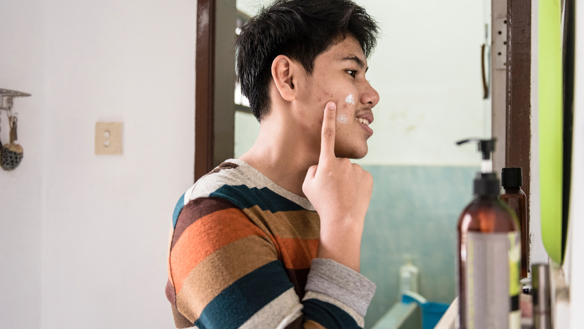 homme appliquant de la crème sur son acné dans le miroir