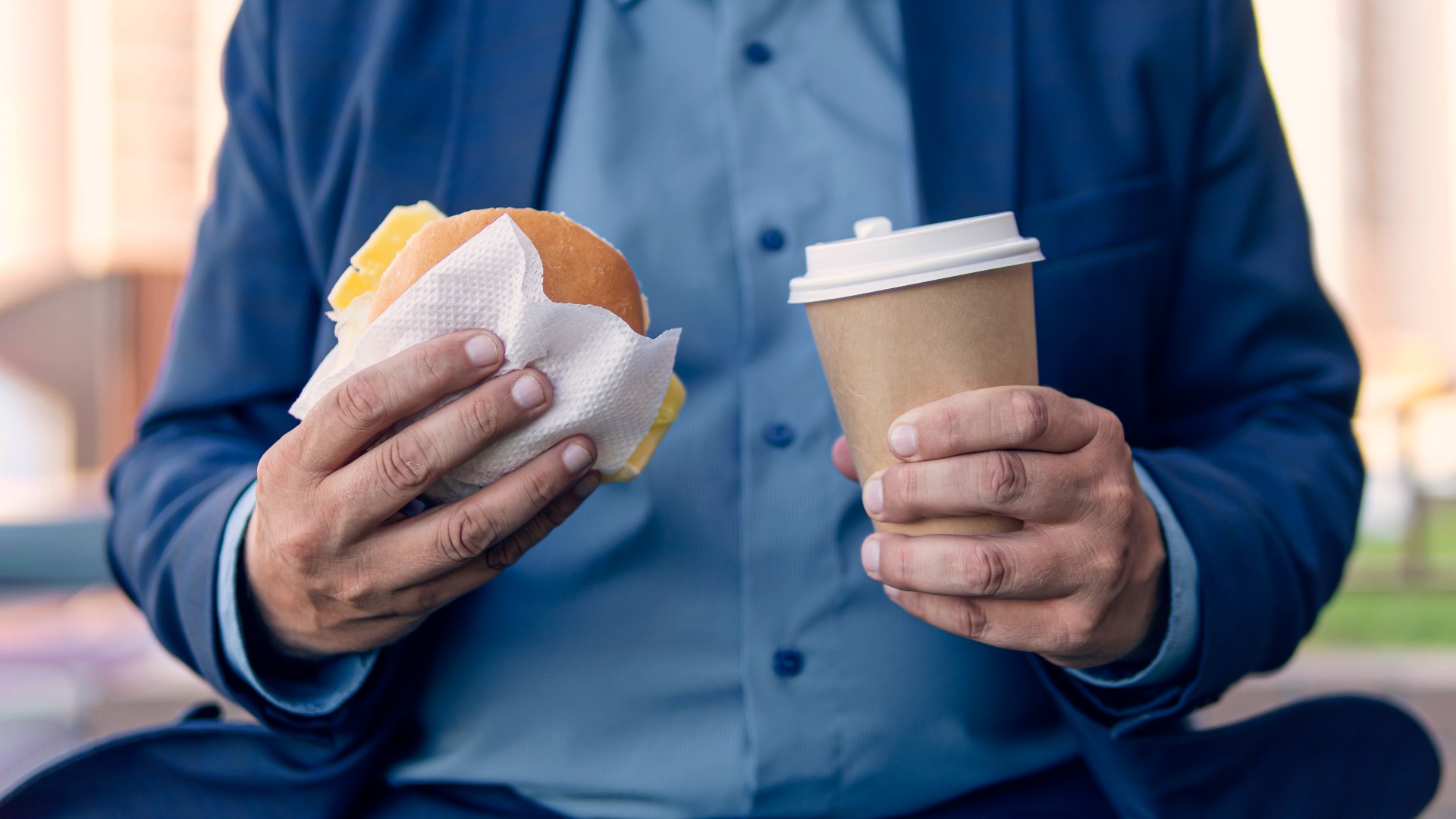 Homme en surpoids tenant un hamburger et un café