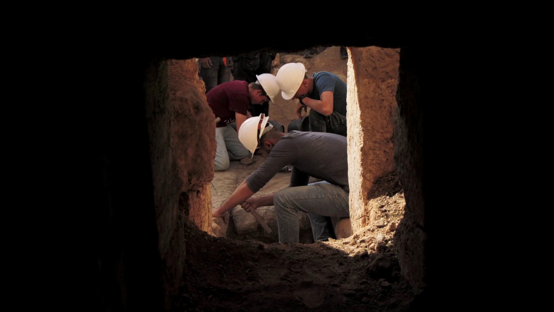 Depuis une grotte, on aperçoit trois archéologues coiffés de casques travaillant sur le site de fouilles de la grotte de Salomé et de son parvis.