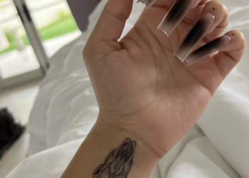 Poignet et main gauches du chat Doja montrant un tatouage de crâne d'antilope et une longue manucure en dégradé