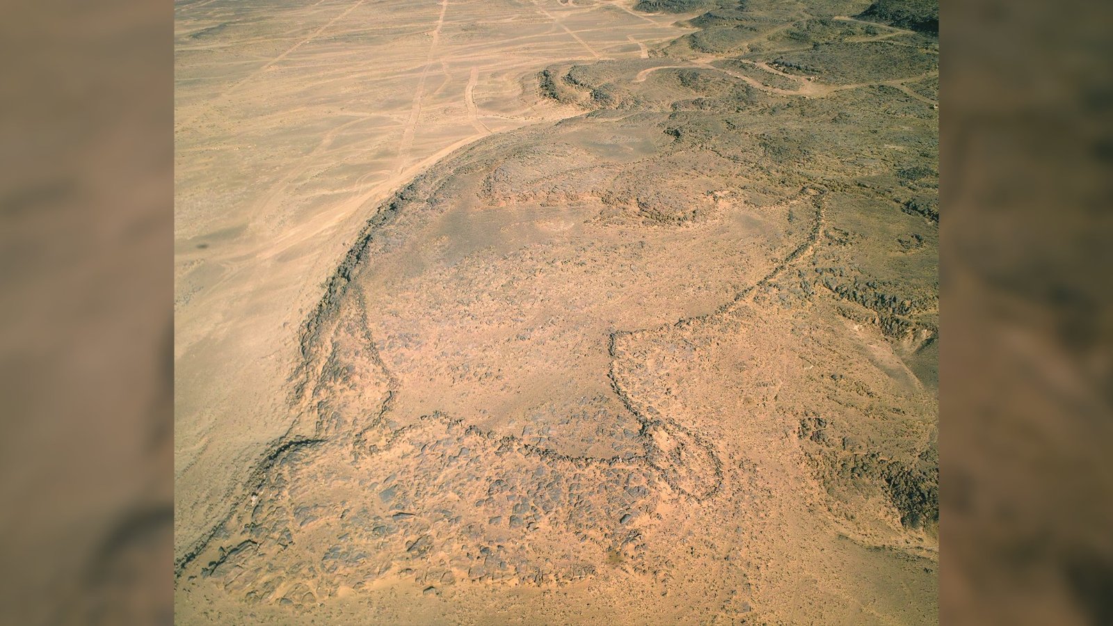 Une vue aérienne d'un cerf-volant du désert.  Nous voyons un grand contour de pierre avec une forme arrondie dans le désert.