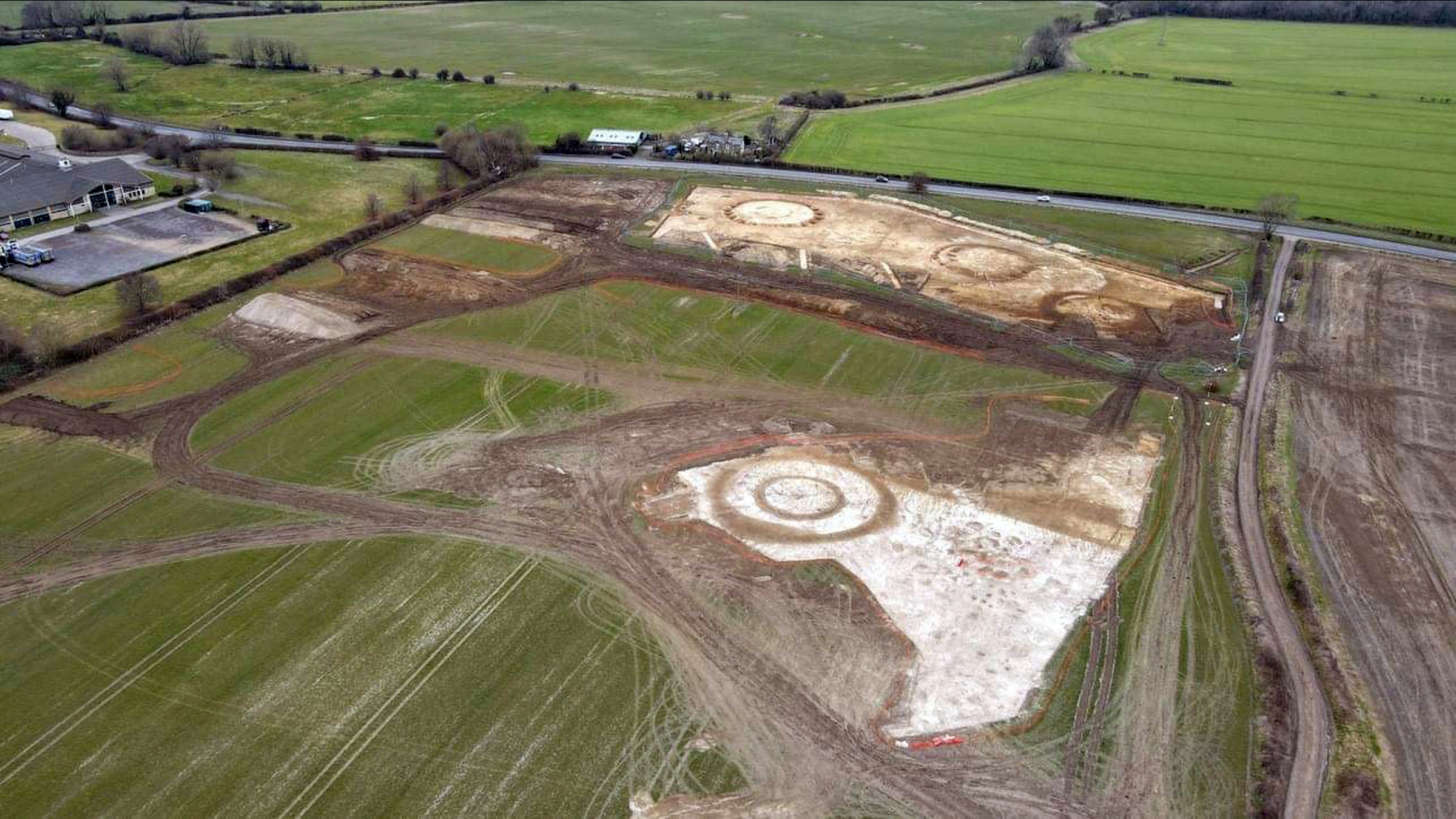 Une vue aérienne du site, qui comprend des champs de terre avec des barres rondes dans un champ vert plus grand à la campagne.