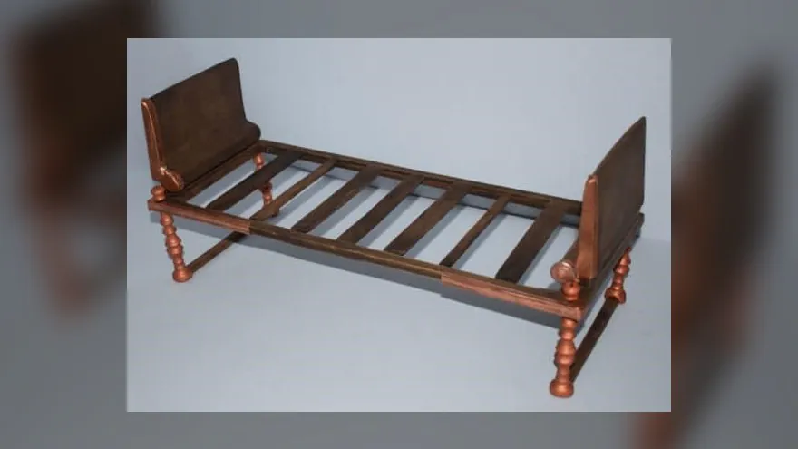 Cette image montre la reconstitution d'un lit en bronze découvert par des archéologues en Grèce. Il est simple et possède un en-tête rectangulaire en bronze aux deux extrémités. Il a plusieurs lattes de bois. Les héritages sont faits de plusieurs morceaux de bronze noueux, mais rien de complexe.