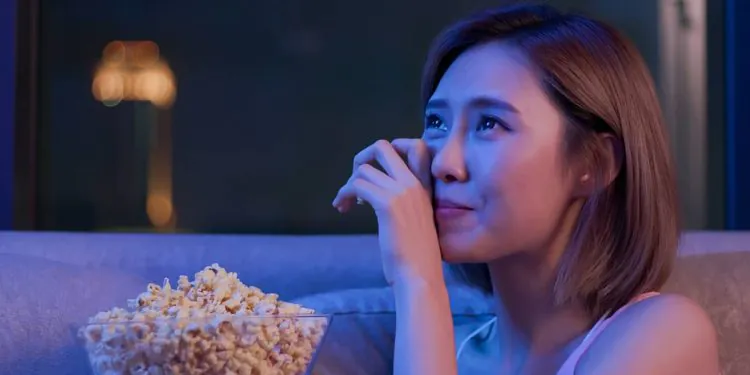 Une jeune femme pleure en regardant un film très émouvant avec du pop-corn la nuit
