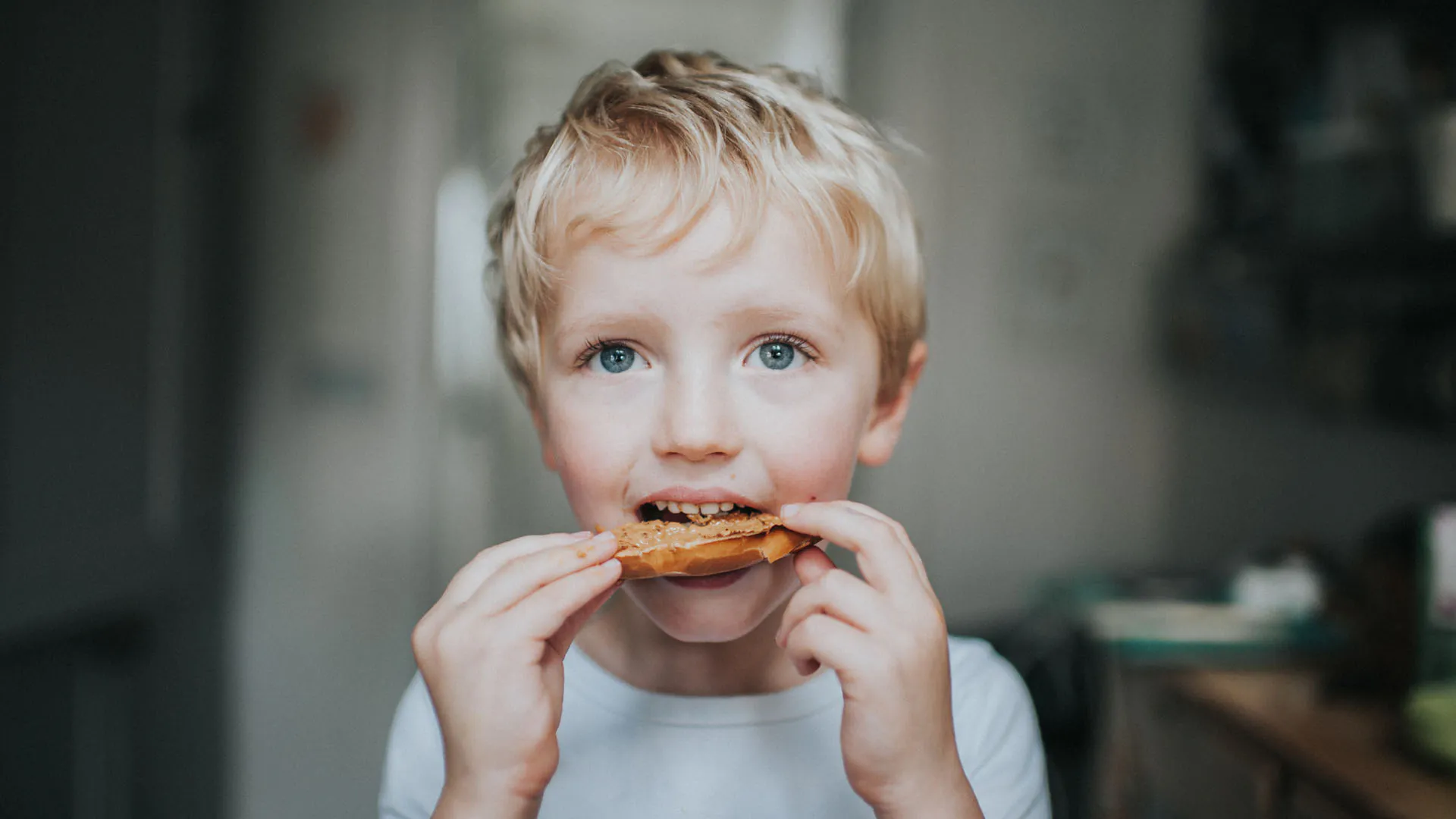 jeune garçon blond mangeant un bagel au beurre de cacahuète
