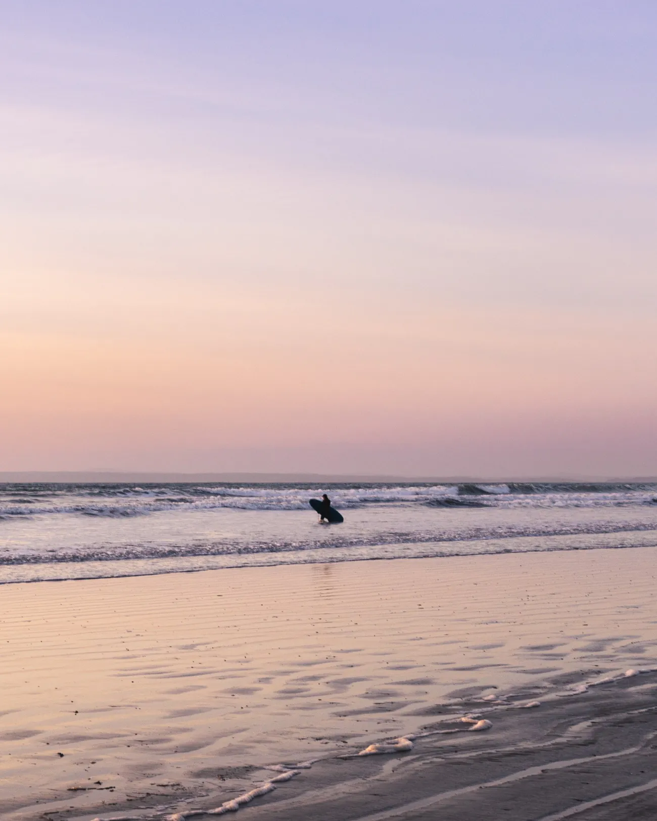 Photo d'un surfeur solitaire lointain debout dans de douces vagues sur la plage.