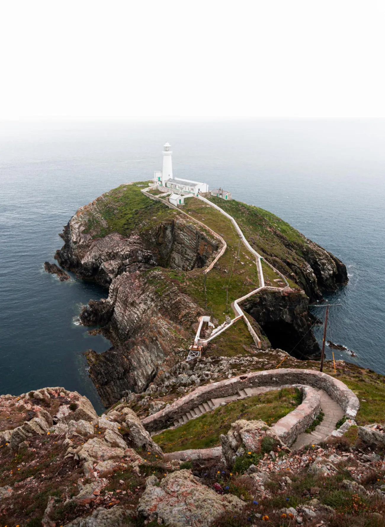 Photo d'un chemin sinueux menant à un phare blanc sur un étroit terrain qui s'avance vers la mer.