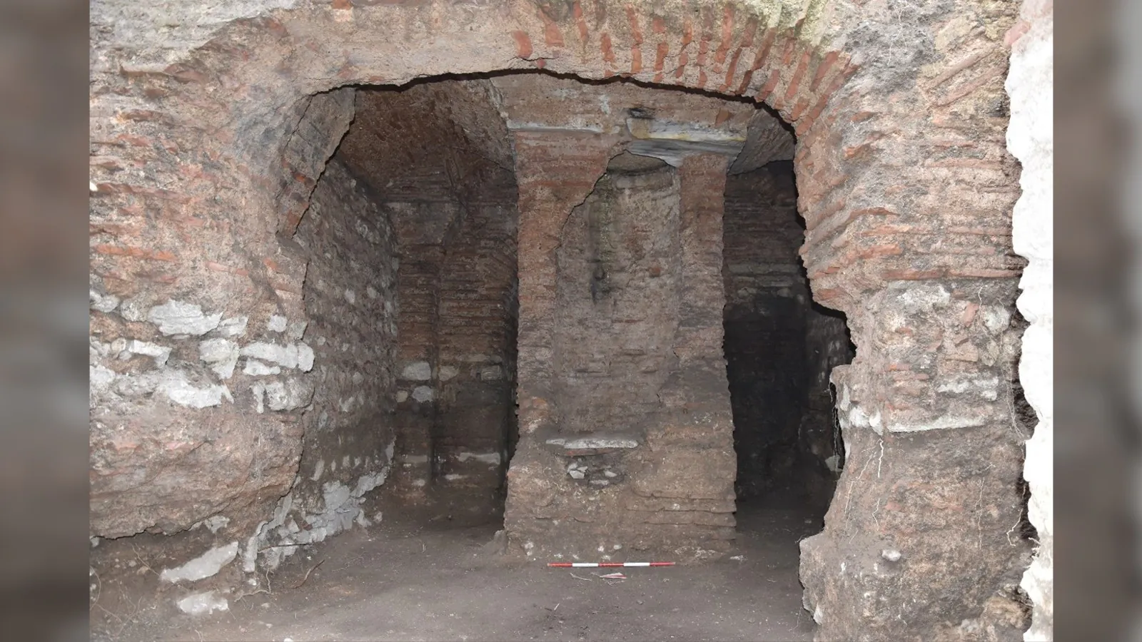 Ici, nous voyons une partie d'une chambre souterraine avec des murs bordés de briques et un pilier au centre de la pièce.